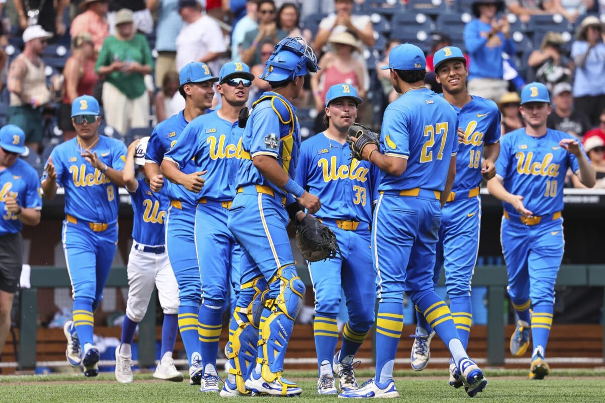 UCLA Bruins baseball players in blue and gold uniforms gather on the field during a College World Series game.