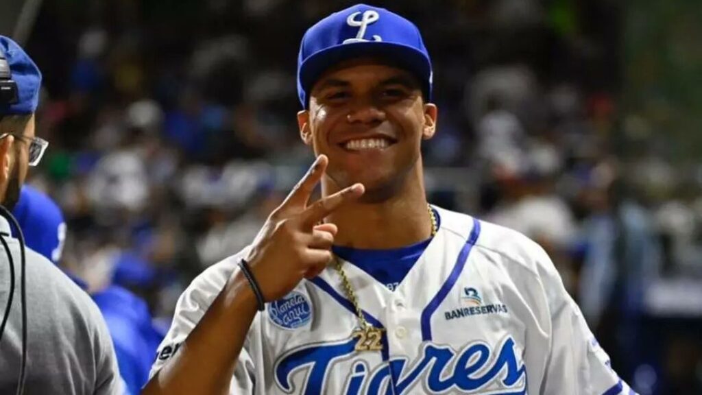 Baseball player smiling and making a peace sign while wearing a Tigres del Licey uniform during a game in the Dominican Republic.