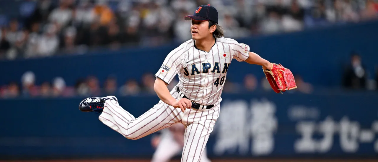 Japanese baseball pitcher delivering a pitch in a Team Japan uniform during an international tournament game.