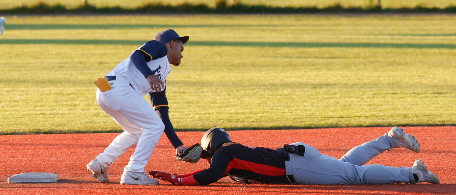 Baseball player applying a tag on a sliding runner at second base during a competitive game