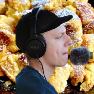 Young man wearing headphones and microphone, focused, with a background of fried food.